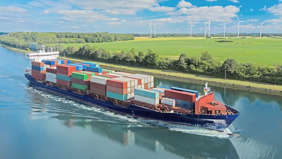 Container ship on the Kiel Canal and windmill on the background.