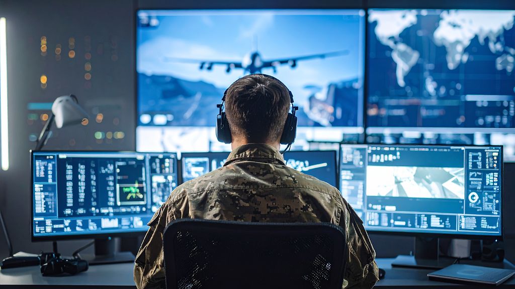 a soldier starring at monitors controlling a drone from a tactical control room. | © AI generated by GTAI with Adobe Firefly a soldier starring at monitors controling a drone from a tactical control room.