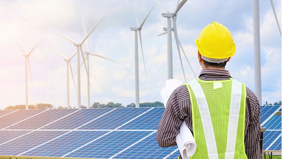 Engineer with yellow helmet on solar module and wind generators.