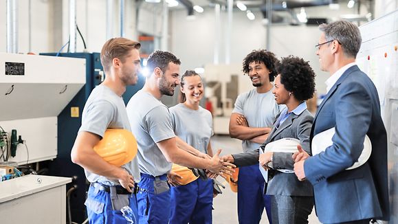 Glueckliche afroamerikanische Geschaeftsfrau, die einem Arbeiter beim Besuch einer Fabrik die Hand schuettelt.