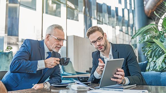 Mature boss and young business man working together using digital tablet in office hall