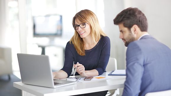 Portrait of investment advisor businesswoman sitting at office in front of computer and consulting with young professional man. 