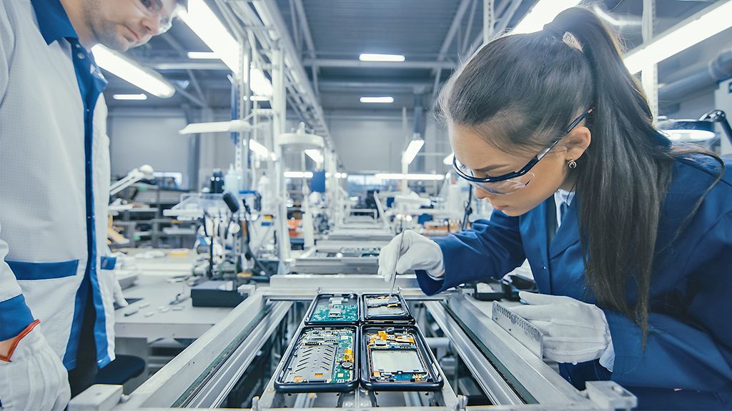 Shot of an Electronics Factory Workers Assembling Circuit Boards by Hand While it Stands on the Assembly Line. High Tech Factory Facility.