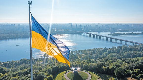 Aerial view of the Ukrainian flag waving in the wind against the city of Kyiv, Ukraine near the famous statue of Motherland.